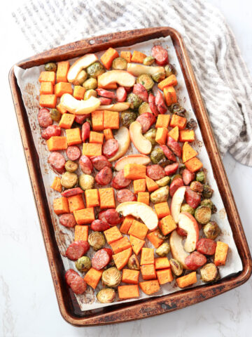 a baking sheet with cut up sausage, apples and vegetables
