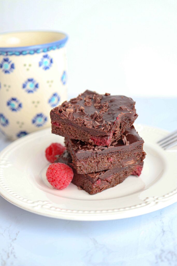 a stack of three avocado brownies on a white plate with a side of raspberries.