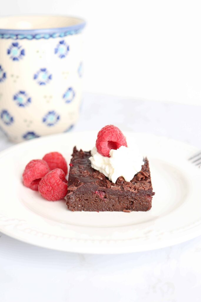 a piece of brownie with whipped cream and raspberries.