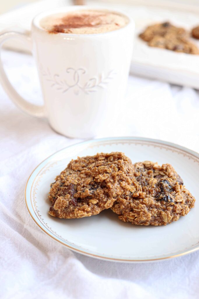 two oatmeal cookies on a plate with a mug of coffee.