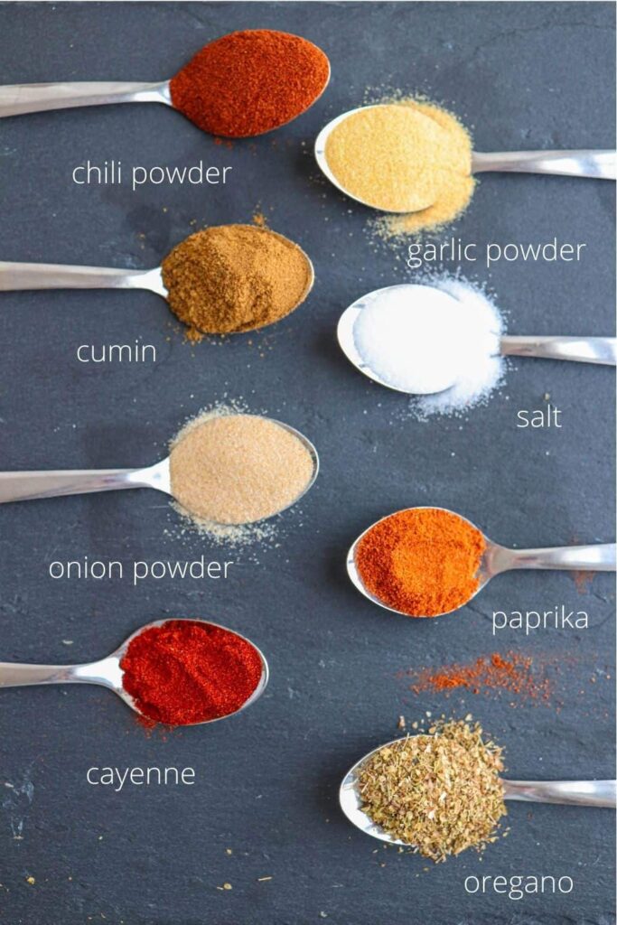 8 spoons with taco seasoning spices on black slate