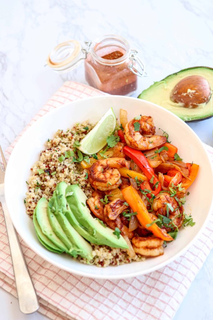 a white bowl with shrimp, peppers, onions, sliced avocado and quinoa