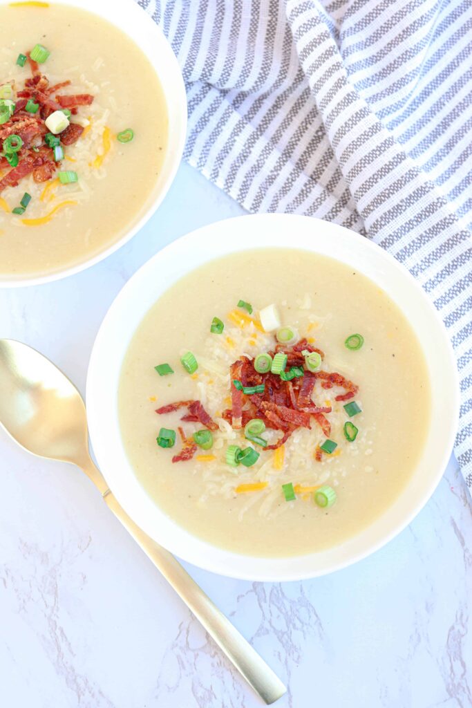 a bowl of creamy potato cauliflower soup on marble countertop with a gold spoon next to it