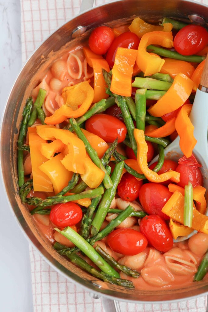 a pot of pasta with sauce, peppers, cherry tomatoes and asparagus