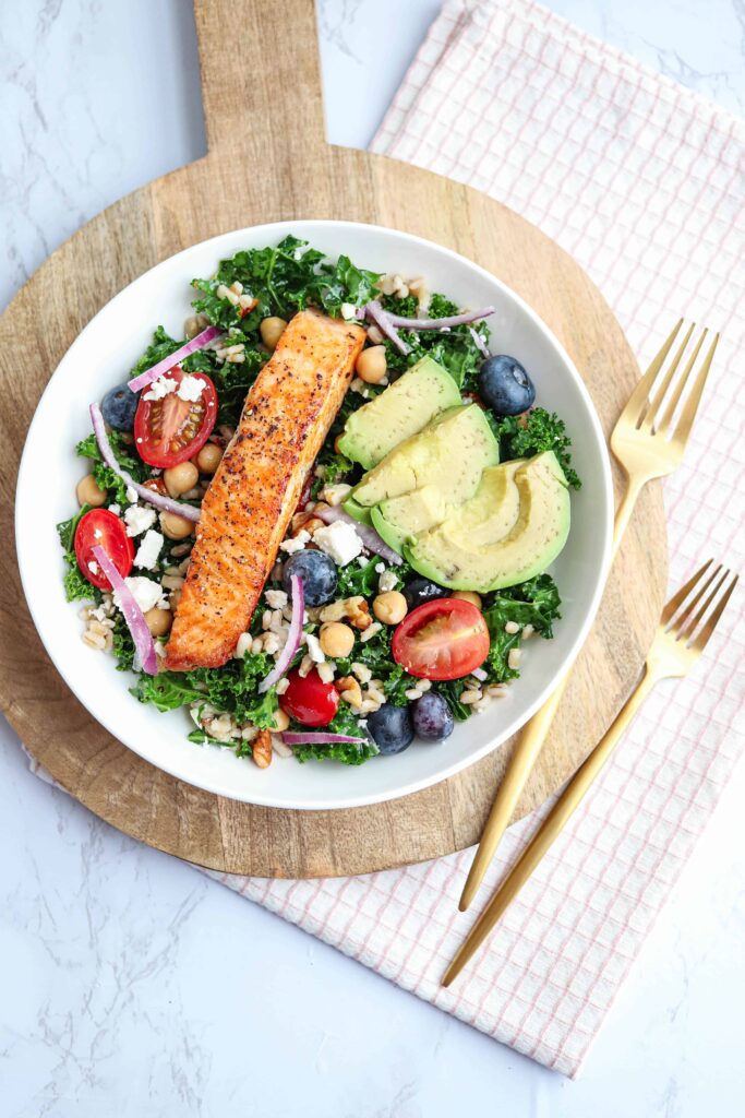 seared salmon kale and barley salad bowl on a wooden board with forks.