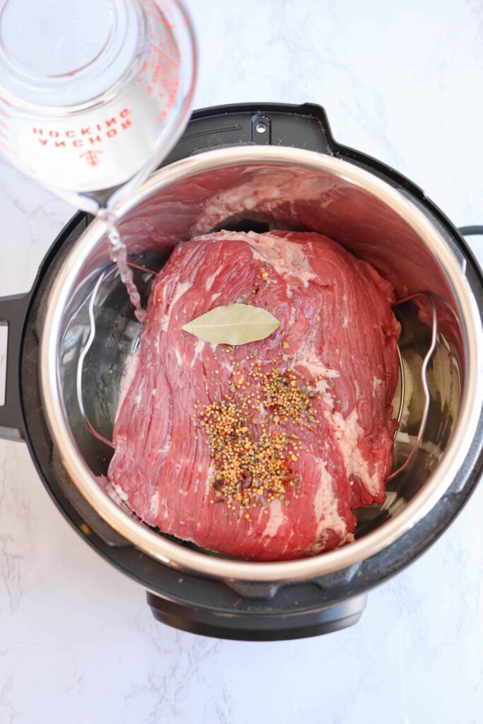 corned beef in an instant pot with water being poured in