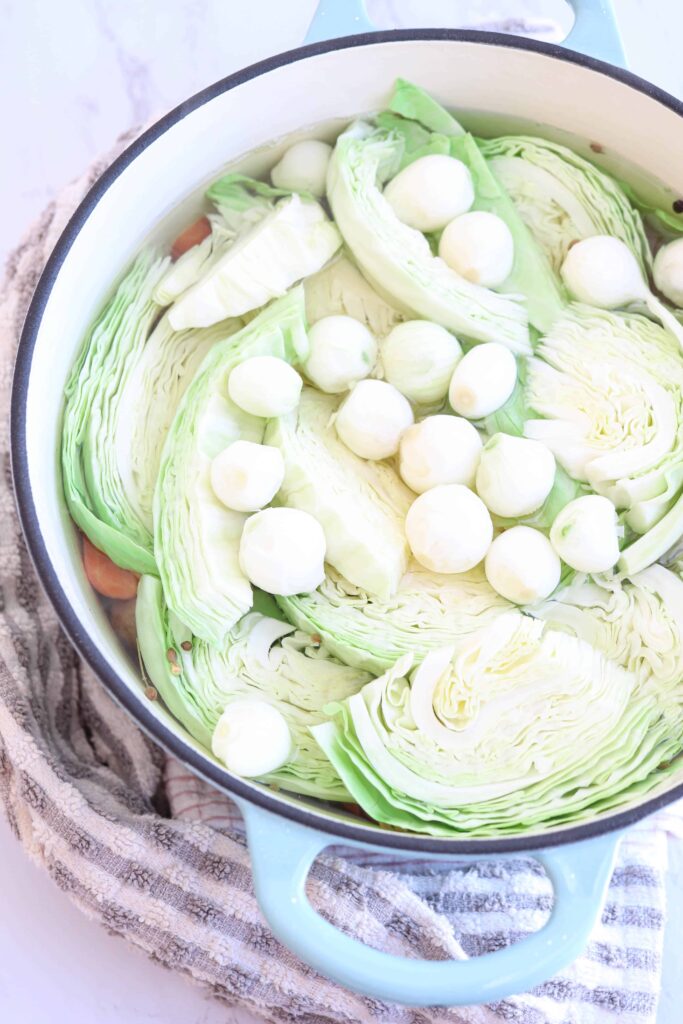 a blue dutch oven with cabbage wedges and pearl onions