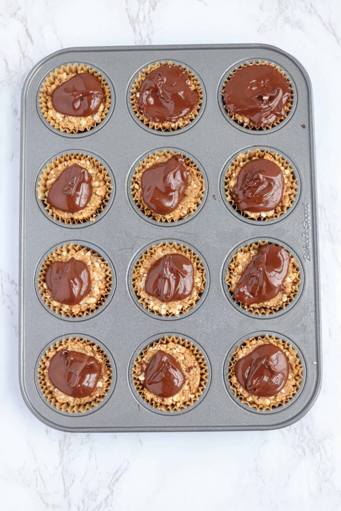 almond butter rice cups in a muffin tin with chocolate melted on top