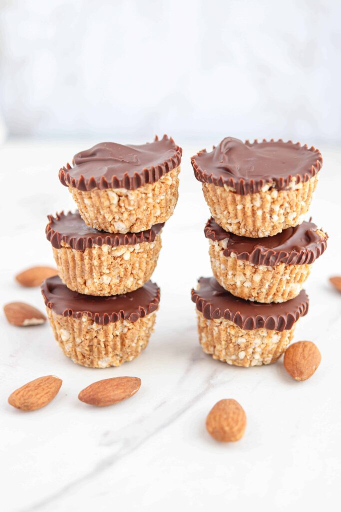 6 almond butter rice cups in 2 stacks of 3 with some almonds on white marble surface