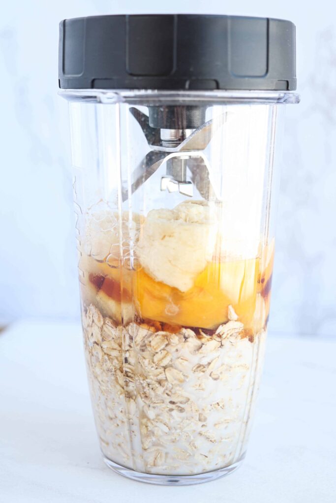 a blender with oats, eggs, banana and vanilla with a lid on white background