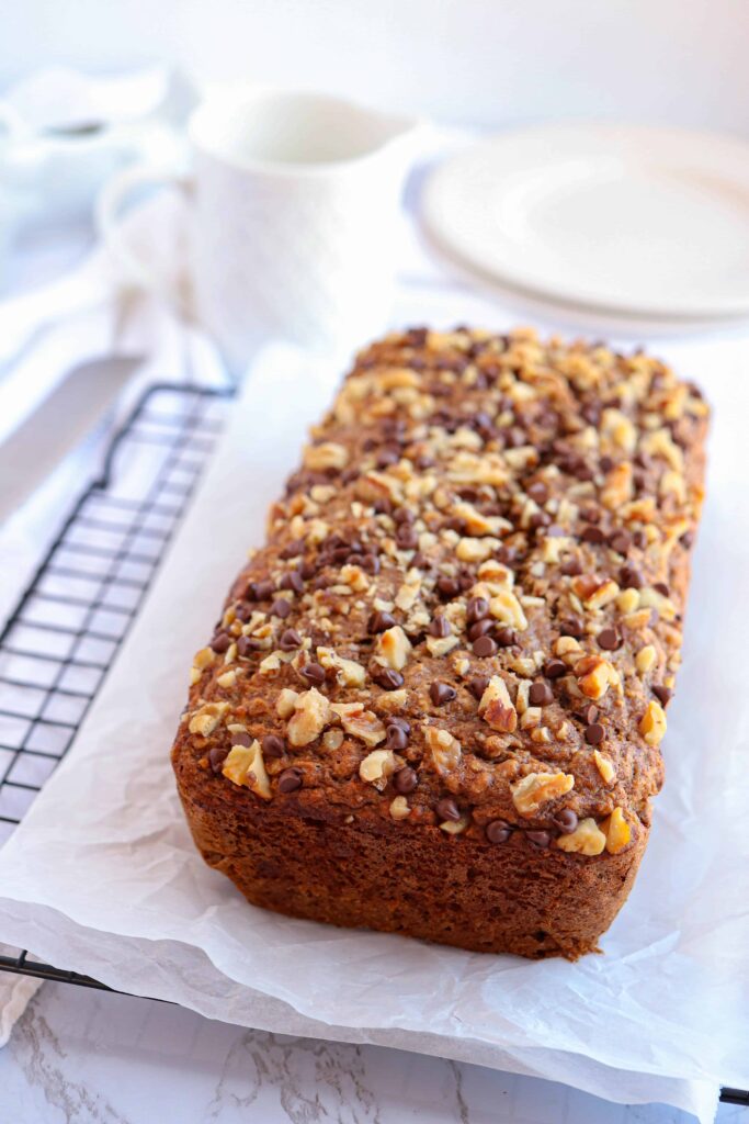 banana bread topped with nuts and mini chocolate chips on paper on a black cooling bread.