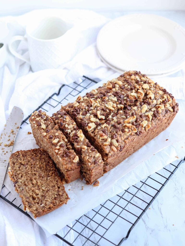 banana bread topped with nuts and mini chocolate chips on paper on a black cooling bread.