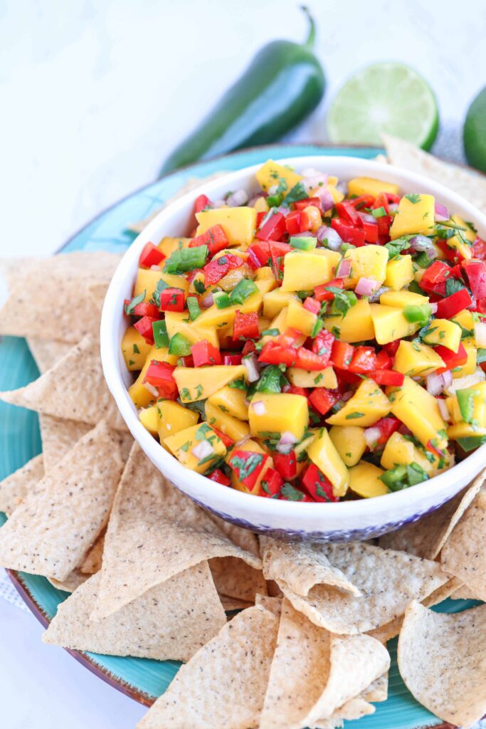 mango salsa in a white bowl surrounded by cassava flour chips on a blue plate