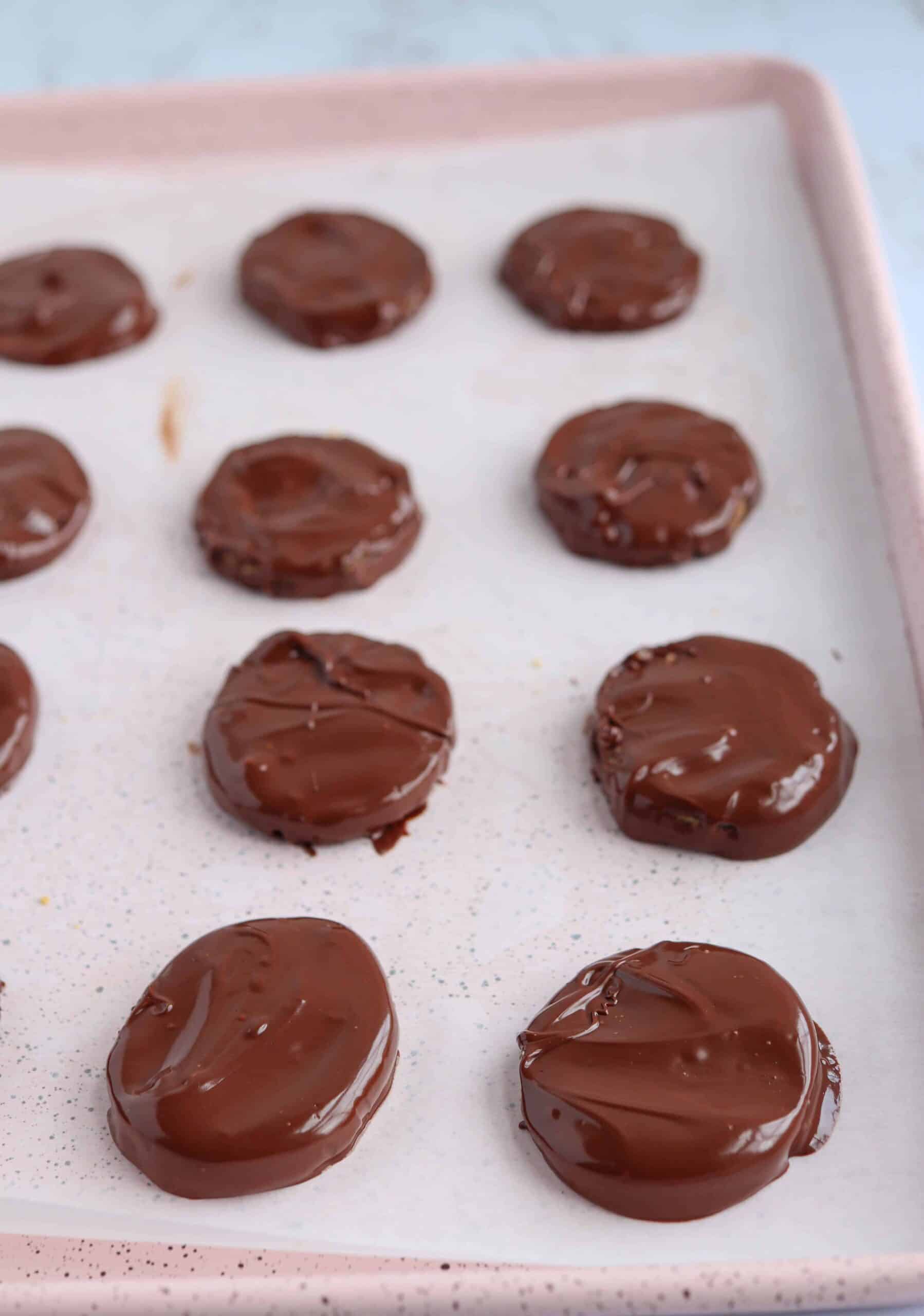 peanut butter eggs dipped in chocolate on a pink baking sheet