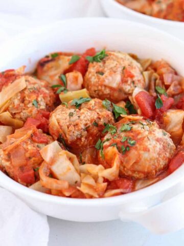 a white bowl with meatballs and cabbage in tomato sauce