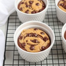 A white ramekin filled with Chocolate Peanut Butter Baked Oats, featuring a swirled pattern of chocolate and light batter, topped with chocolate chips, placed on a cooling rack.
