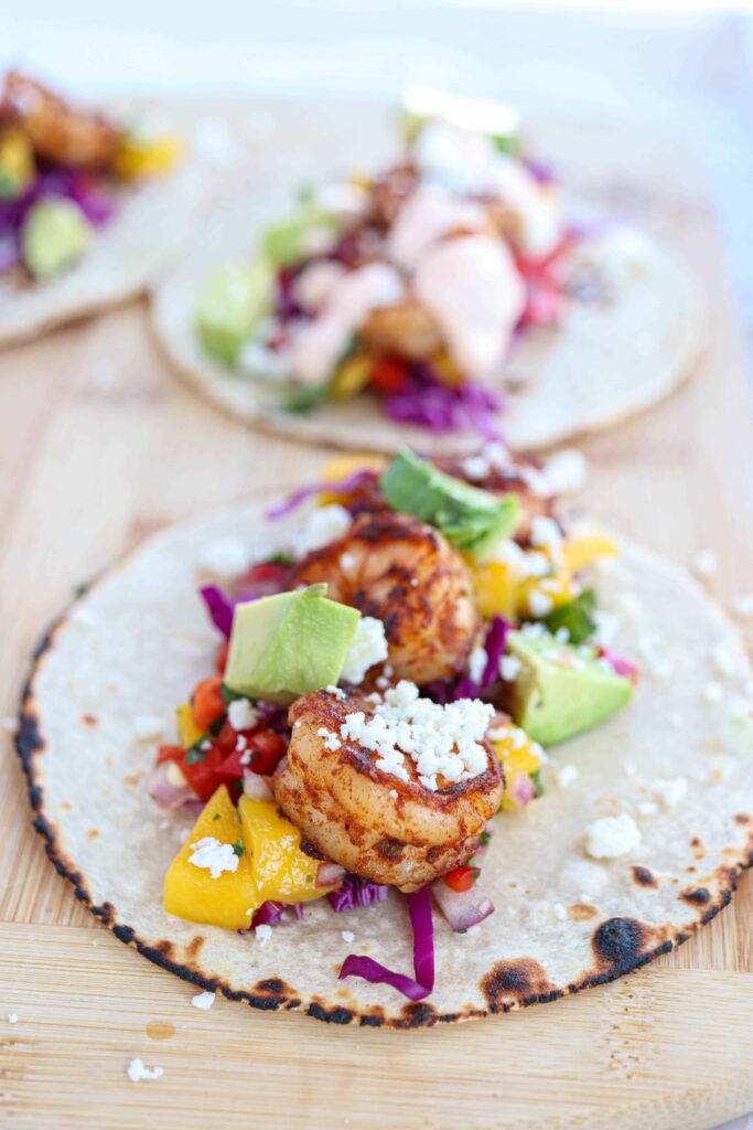 corn tortilla with charred edges, topped with shrimp, avocado and mango salsa on a wooden board