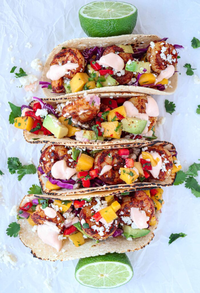 4 shrimp tacos with mango salsa, avocado, cilantro, Cotija cheese on white paper