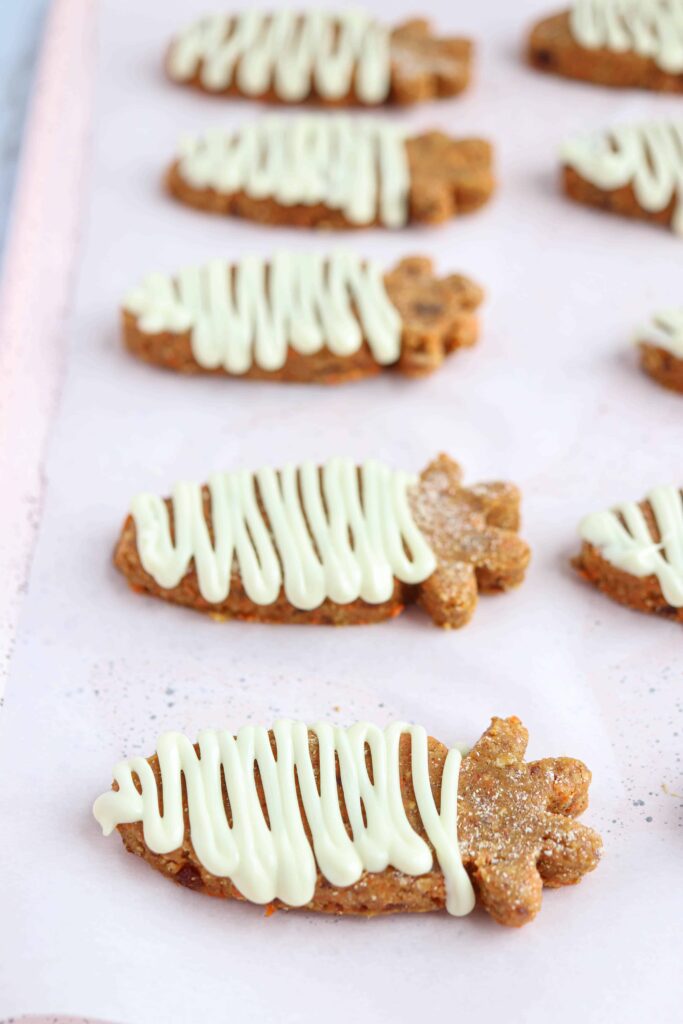 carrot shaped carrot cake no bake cookies with white chocolate drizzle on white paper in a row