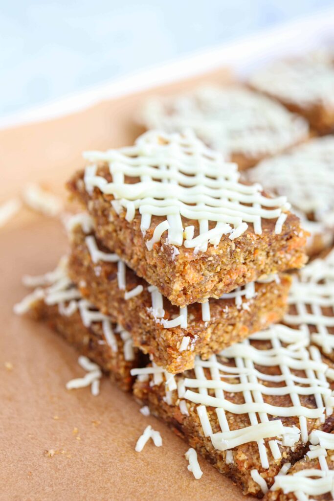 no bake carrot cake bars with white chocolate drizzle on brown paper stacked to show structure