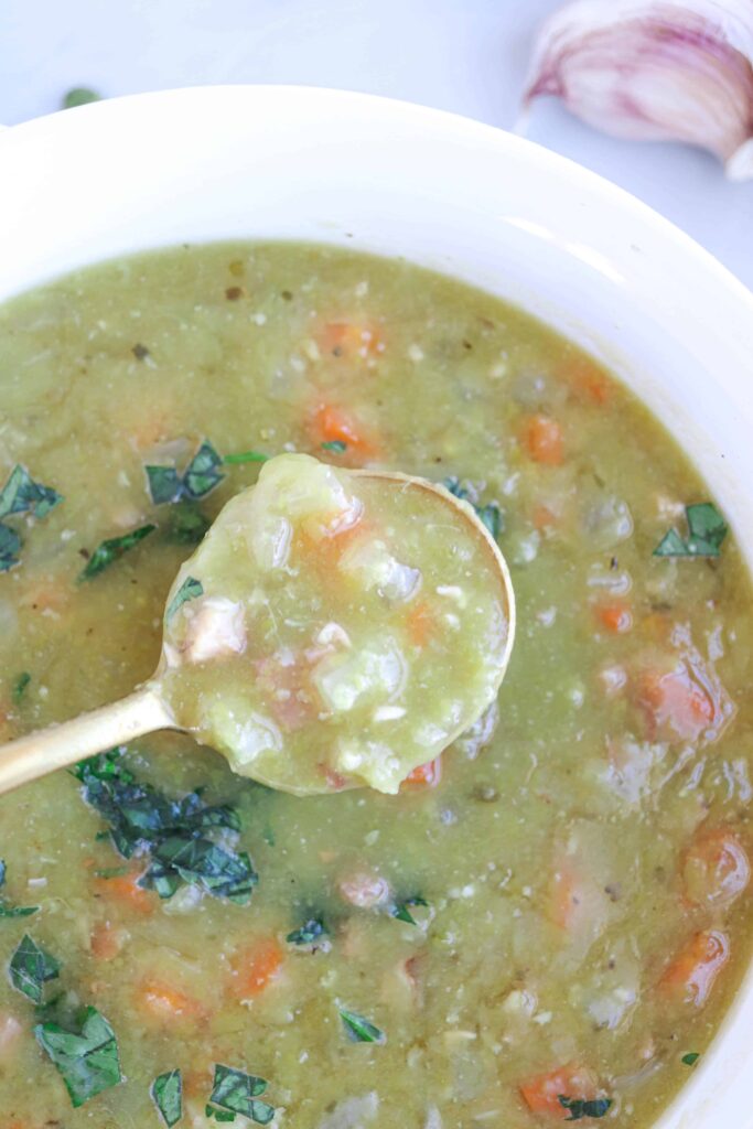 close up of split pea and ham soup in a white bowl with a gold spoon showing soup's texture.