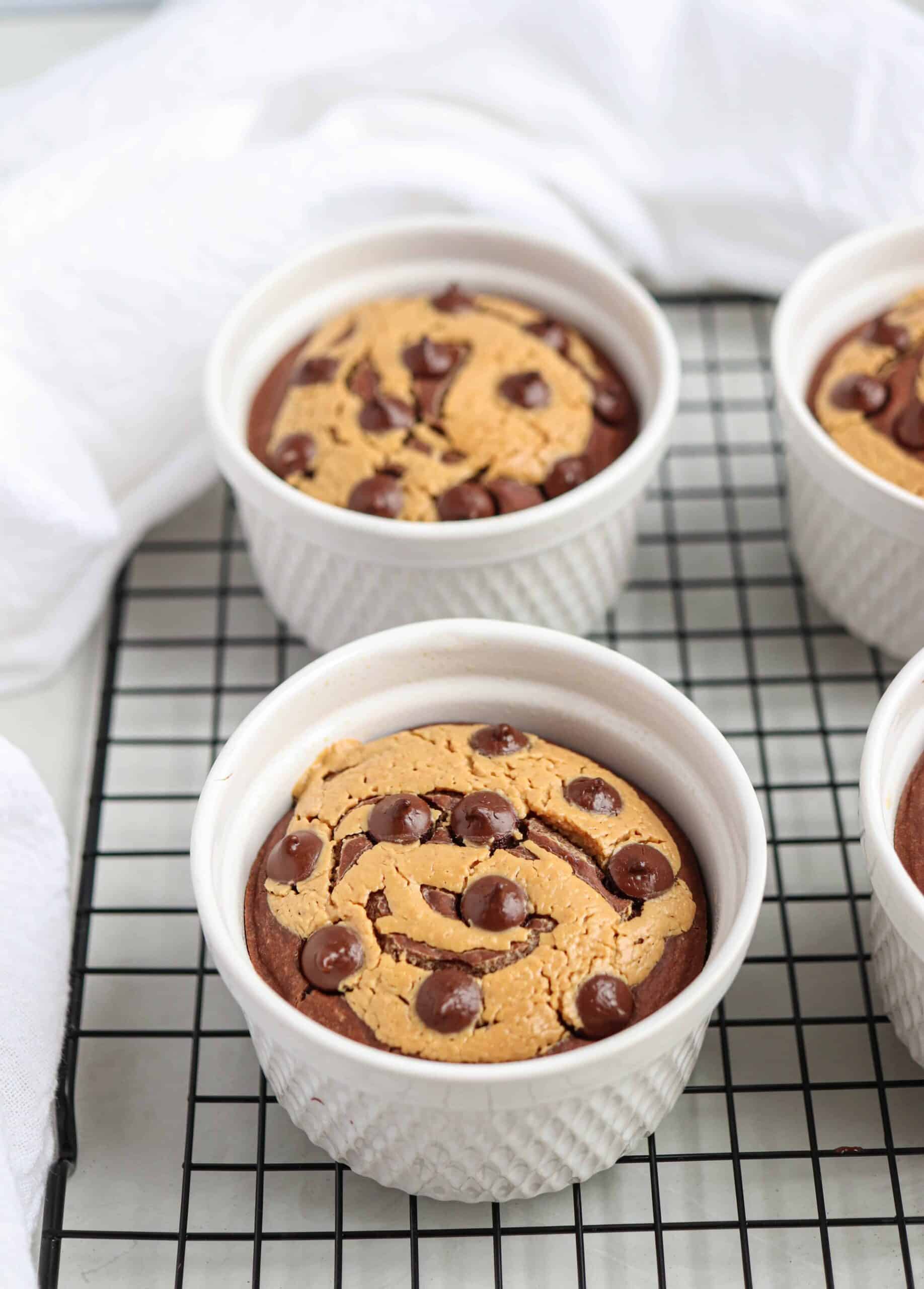 four white ramekins on a black cooling rack with chocolate peanut butter baked oats, 2 ramekins cut off