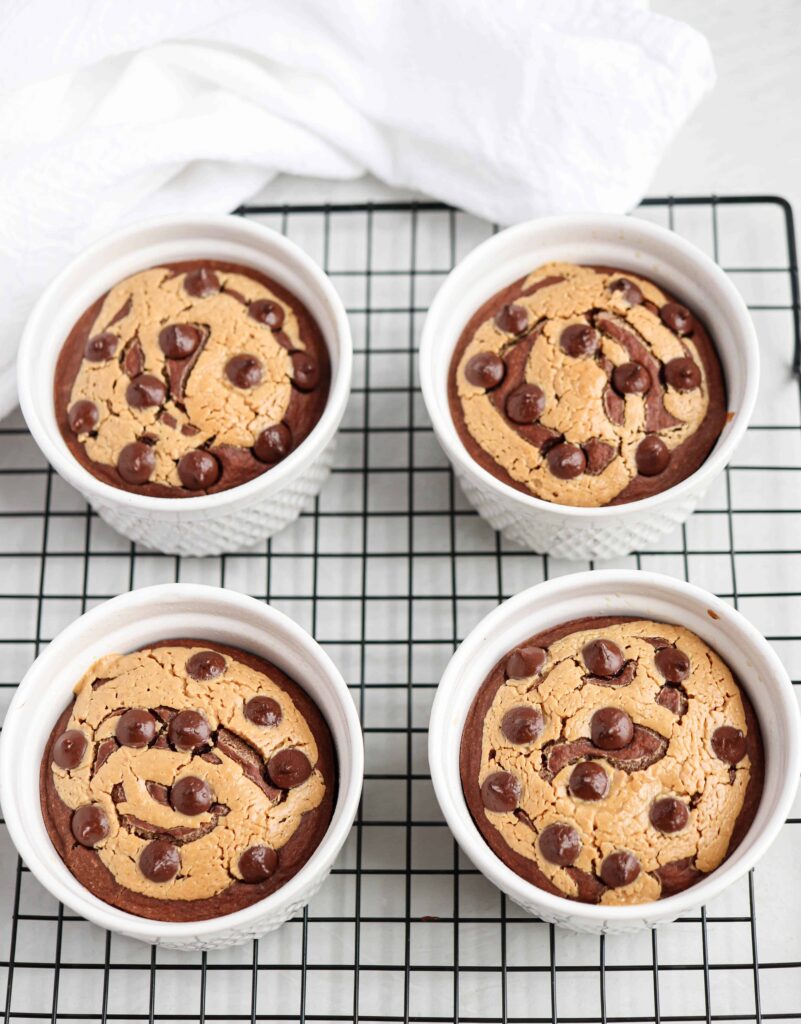 four ramekins with chocolate peanut butter baked oats on a black cooling rack with a white kitchen towel in the back.