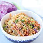 A colorful, easy Egg roll in a bowl featuring shredded cabbage, carrots, green onions, and crumbled tofu topped with an orange sauce. Presented in a patterned white bowl with red cabbage peeking in the background.