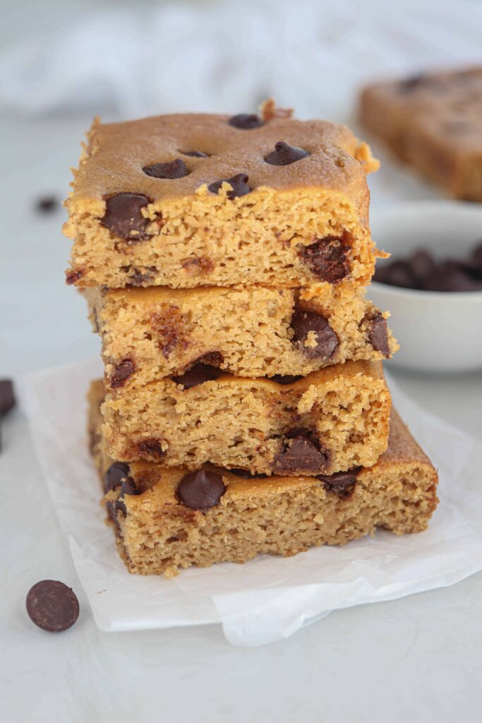 four chickpea blondies stacked on white parchment paper.