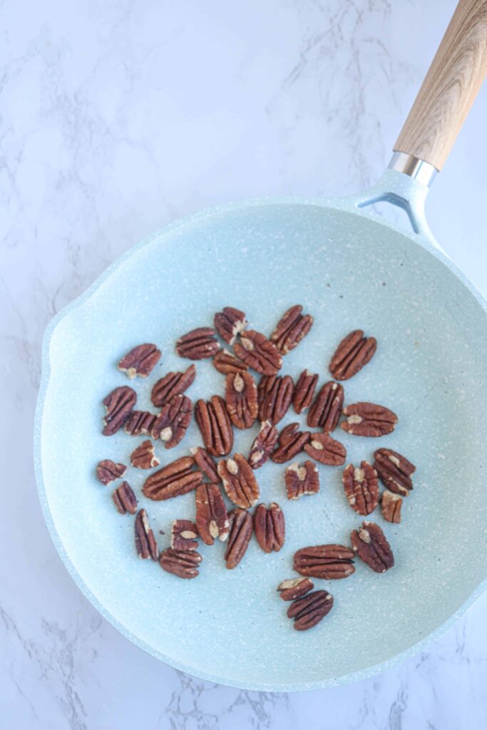 pecan halves in a light blue skillet on white marble surface