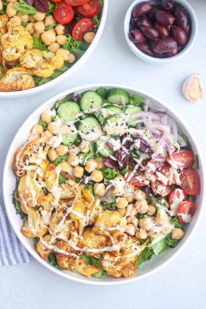 cauliflower shawarma bowl in a white bowl with veggies and tahini sauce.