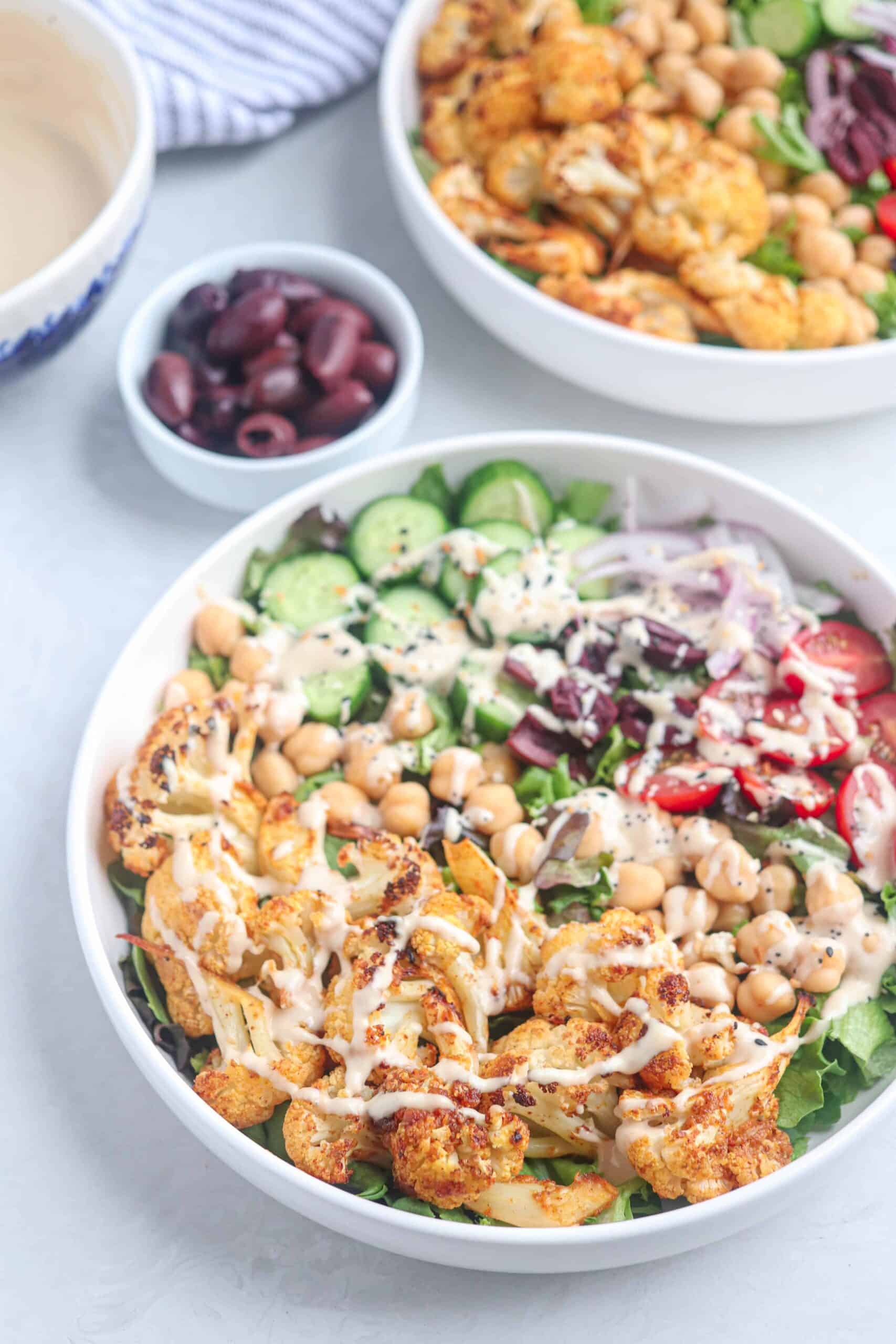 cauliflower shawarma bowl in a white bowl with veggies and tahini sauce.
