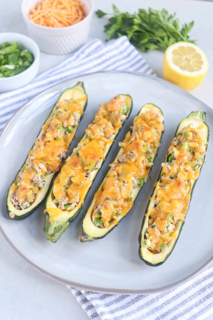 four zucchini boats filled with tuna salad and melted cheese on a gray plate.