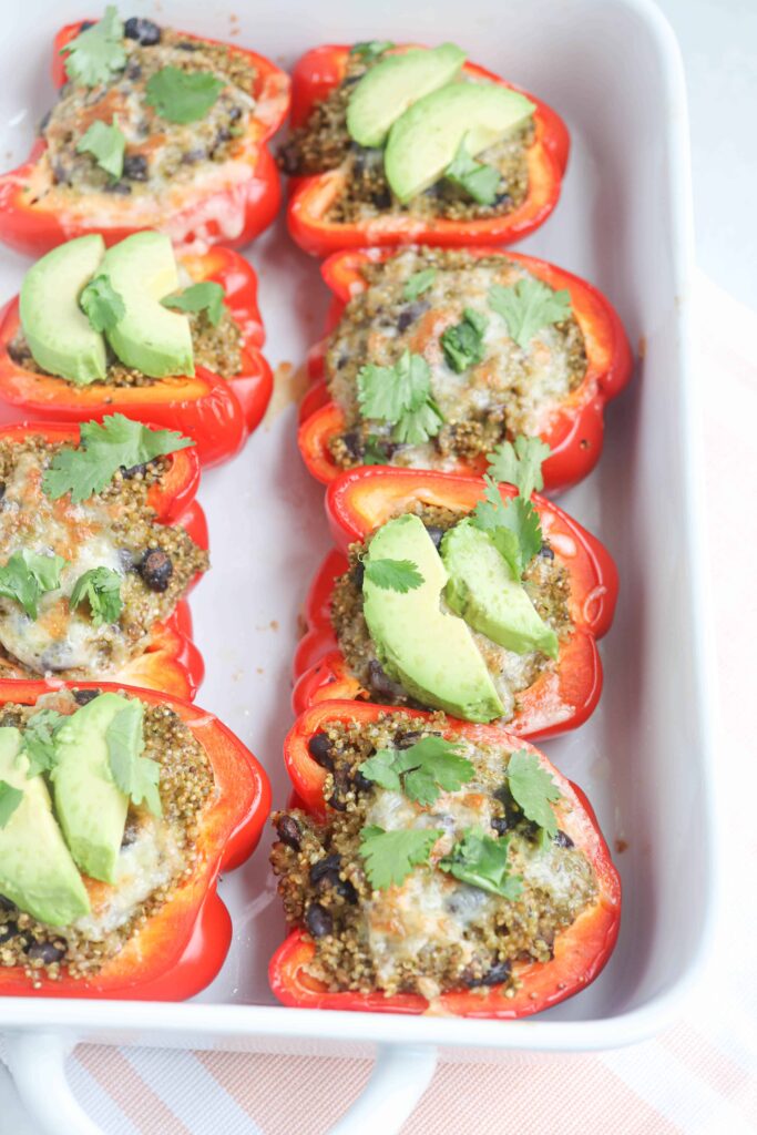 mexican quinoa stuffed red peppers with avocado and fresh cilantro in a casserole dish.