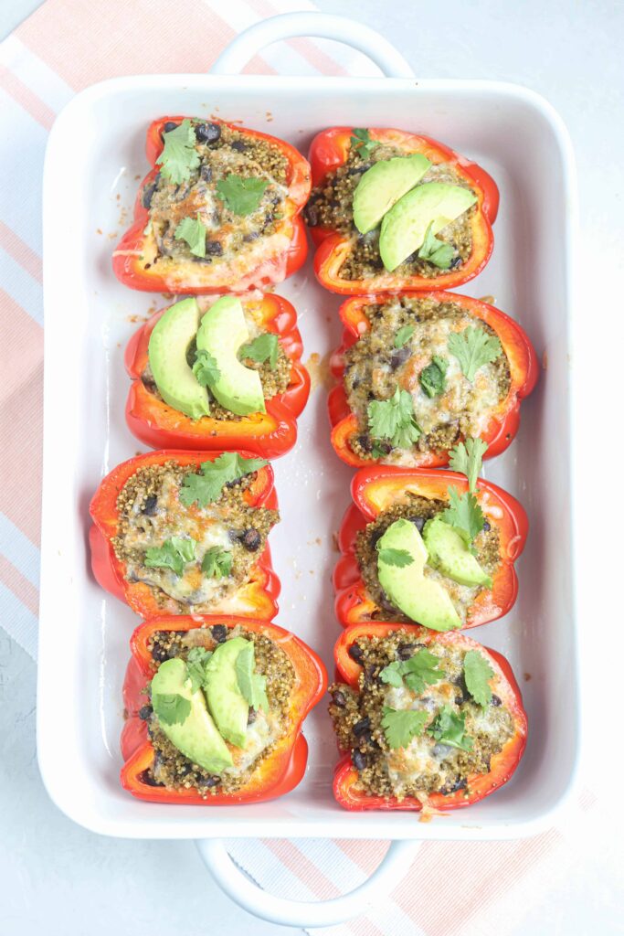 mexican quinoa stuffed red peppers with avocado and fresh cilantro in a casserole dish.