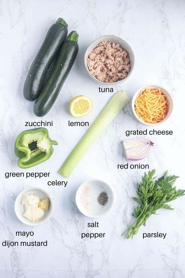 ingredients for making zucchini boats stuffed with tuna on white marble surface with captions. 