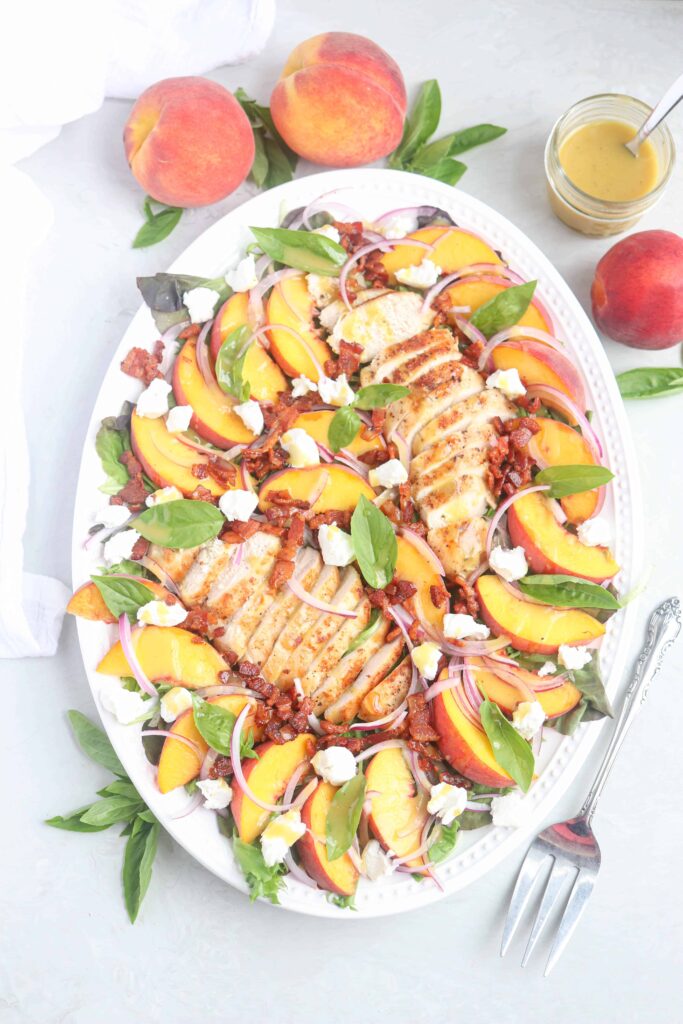chicken peach salad with bacon and goat cheese on an oval platter.