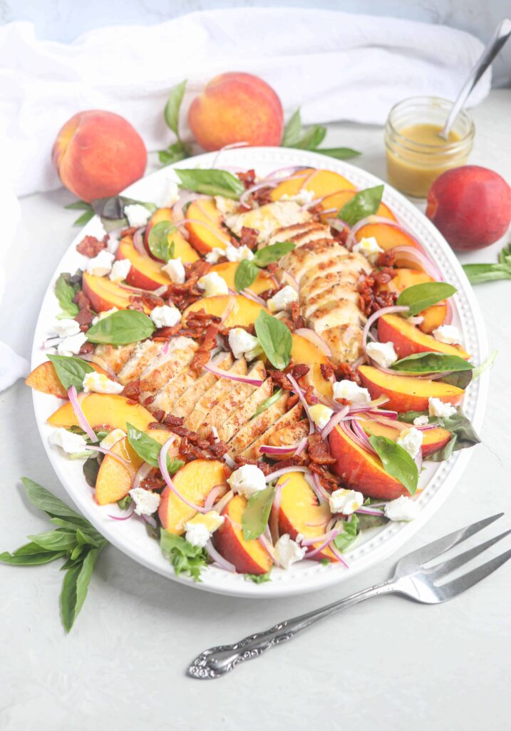 chicken peach salad with bacon and goat cheese on an oval platter.