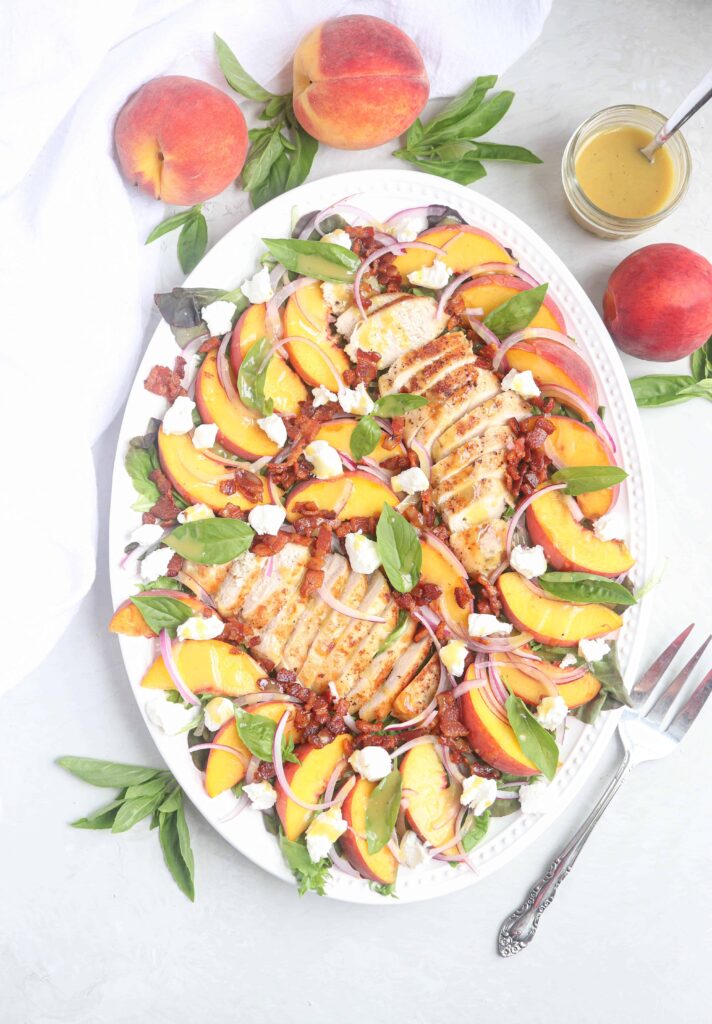 chicken peach salad with bacon and goat cheese on an oval platter.