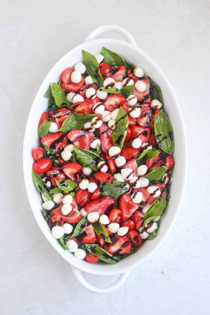strawberry spinach caprese salad served in an oval casserole dish on light gray surface 