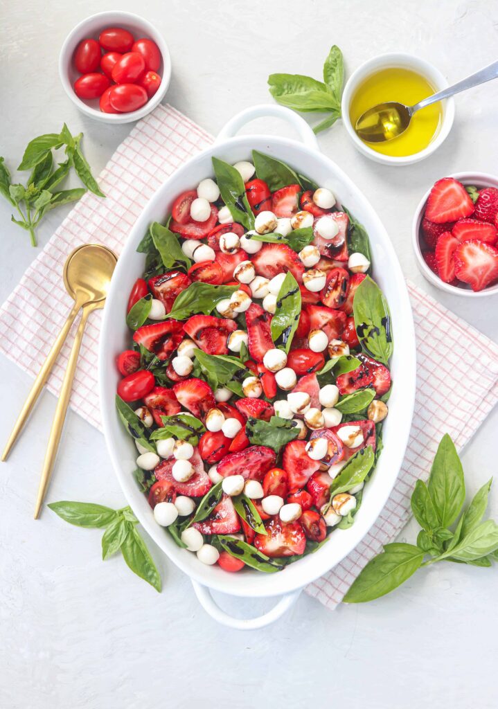 strawberry spinach caprese salad served in an oval casserole dish on light gray surface on a red a white kitchen towel
