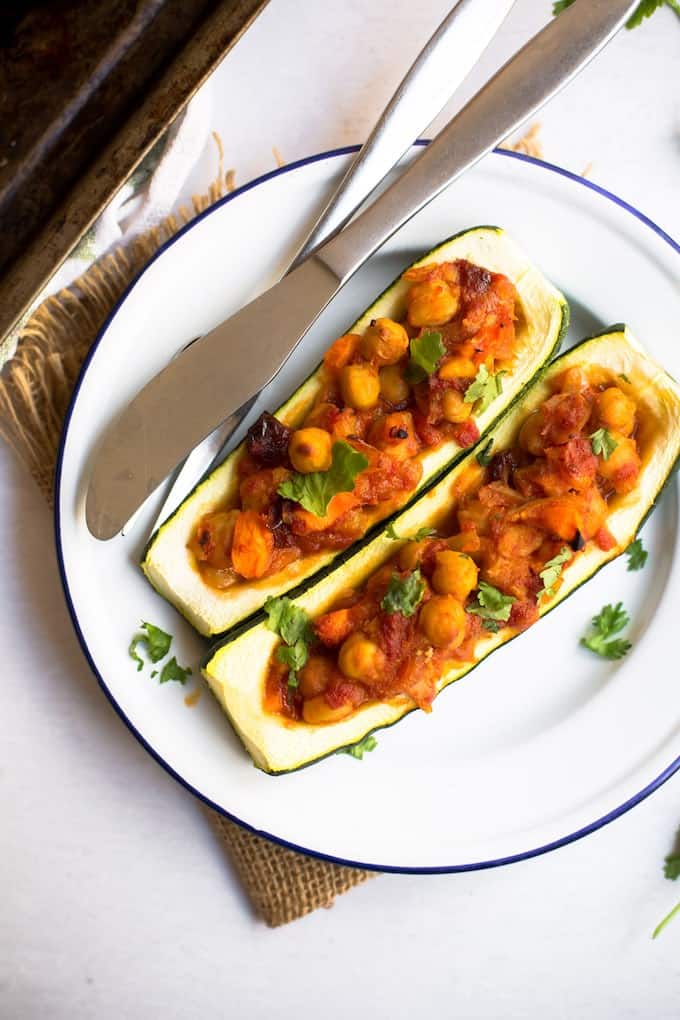 two zucchini boats stuffed with chickpeas and tomatoes on a plate.