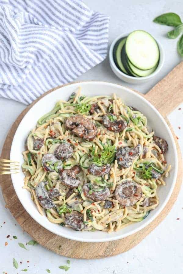a white bowl with creamy zucchini mushroom spaghetti on a round wooden board