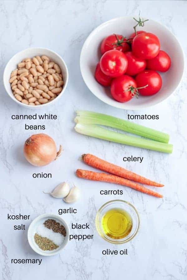 tomato and bean soup ingredients before cooking laid out on a white marble countertop with labels.
