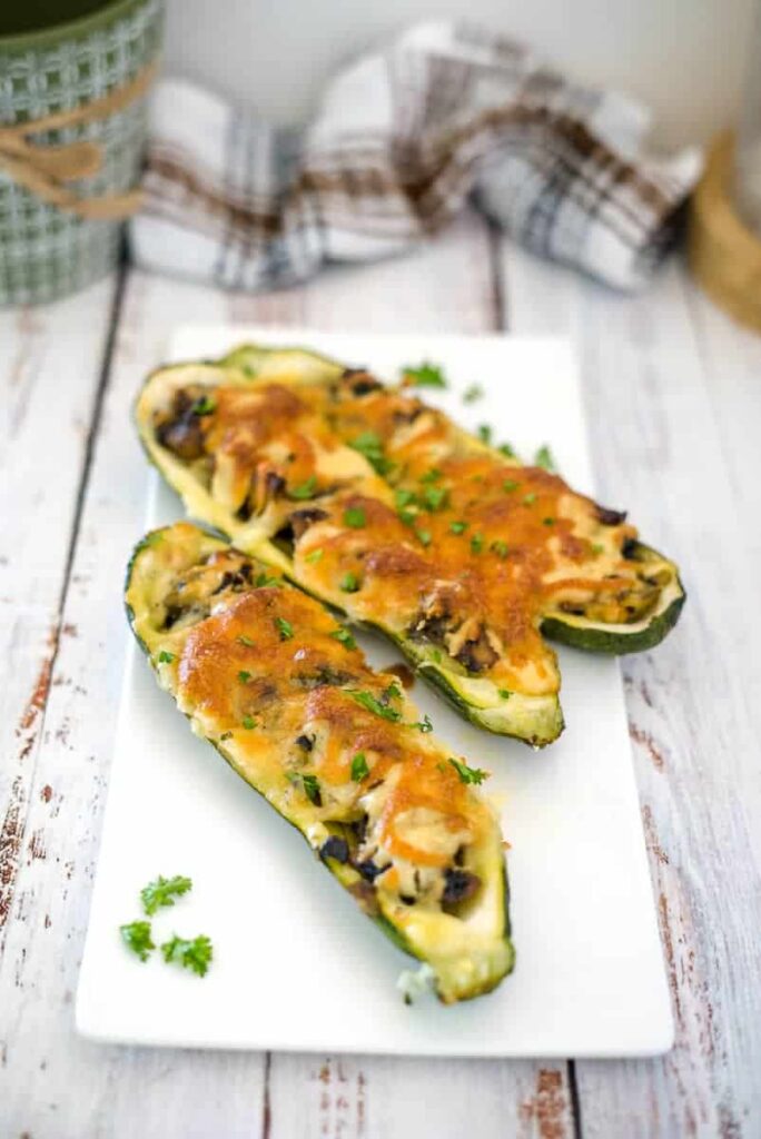 mushroom and cheese stuffed zucchini boats on a white board.