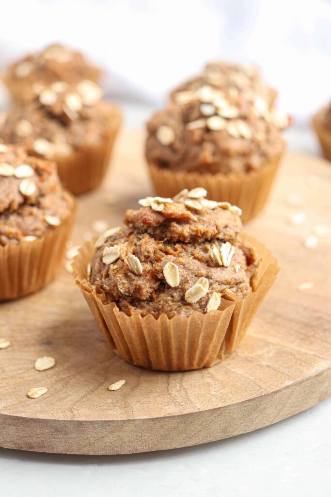 banana carrot oat muffins on a round wooden board on light gray surface.