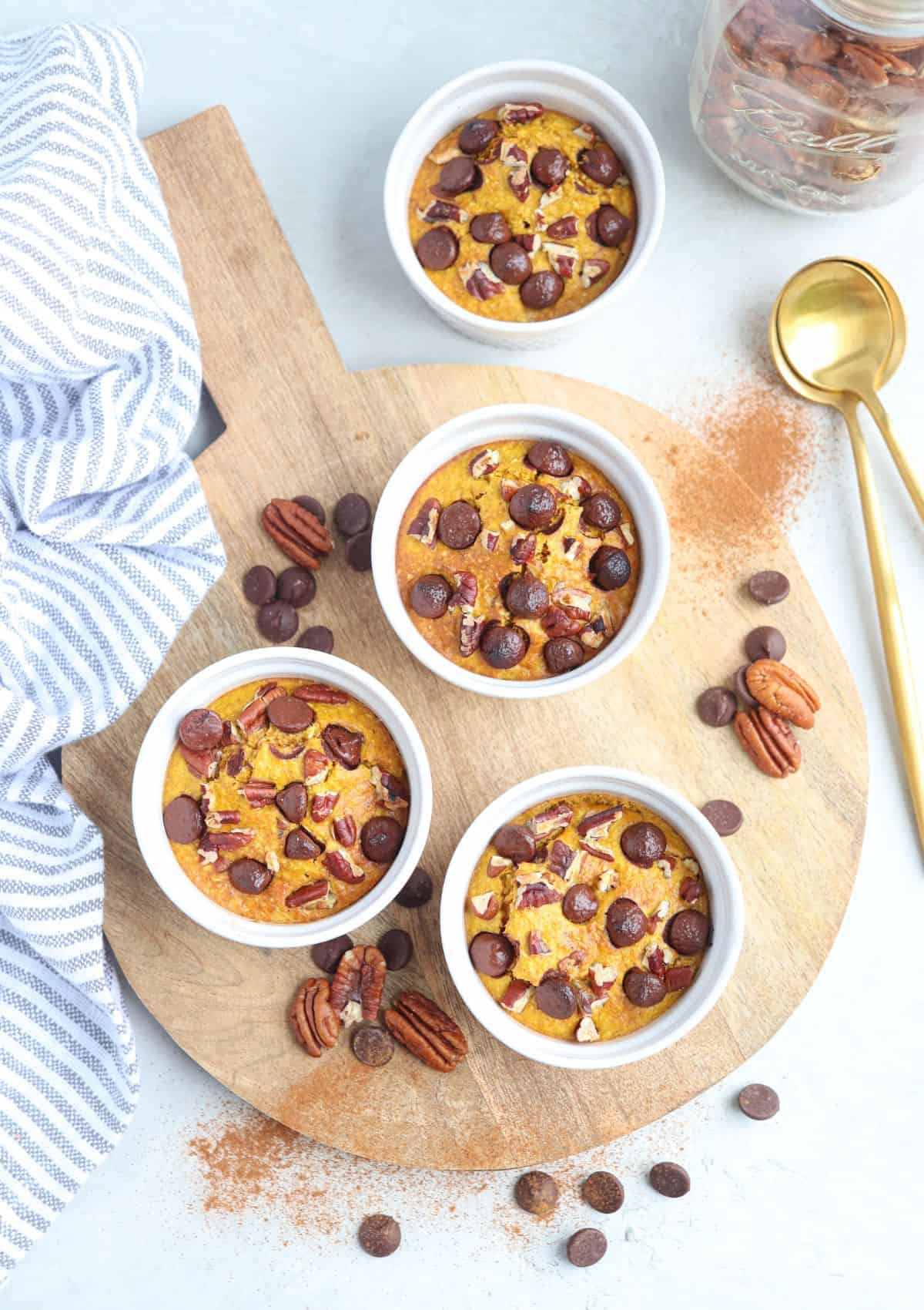 pumpkin blended baked oats in three white ramekins on a round wooden board.