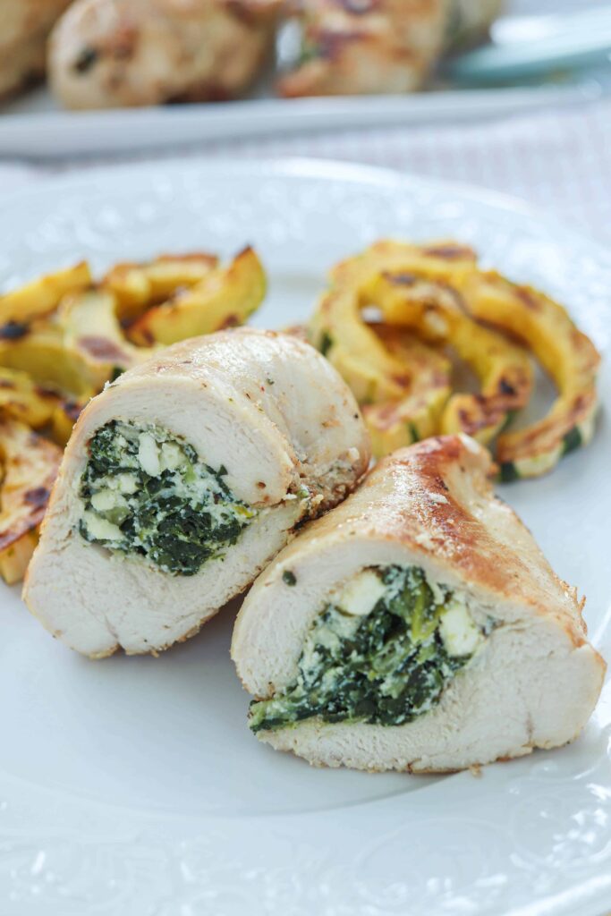 chicken breast stuffed with spinach and cheese cut in half with a side of roasted squash.