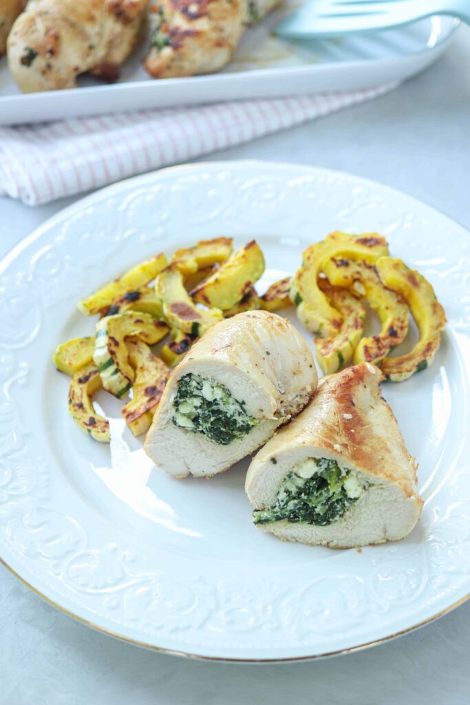 chicken breast stuffed with spinach and cheese cut in half with a side of roasted squash.