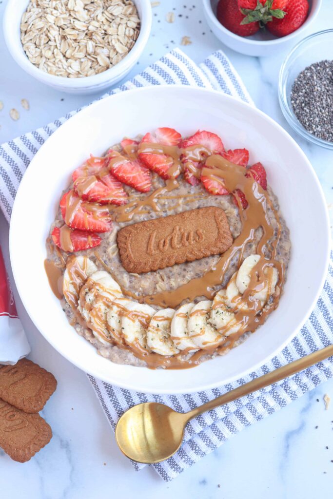 Biscoff oatmeal in a white bowl with strawberries, bananas, one Biscoff cookie and a drizzle of Biscoff cookie spread on top